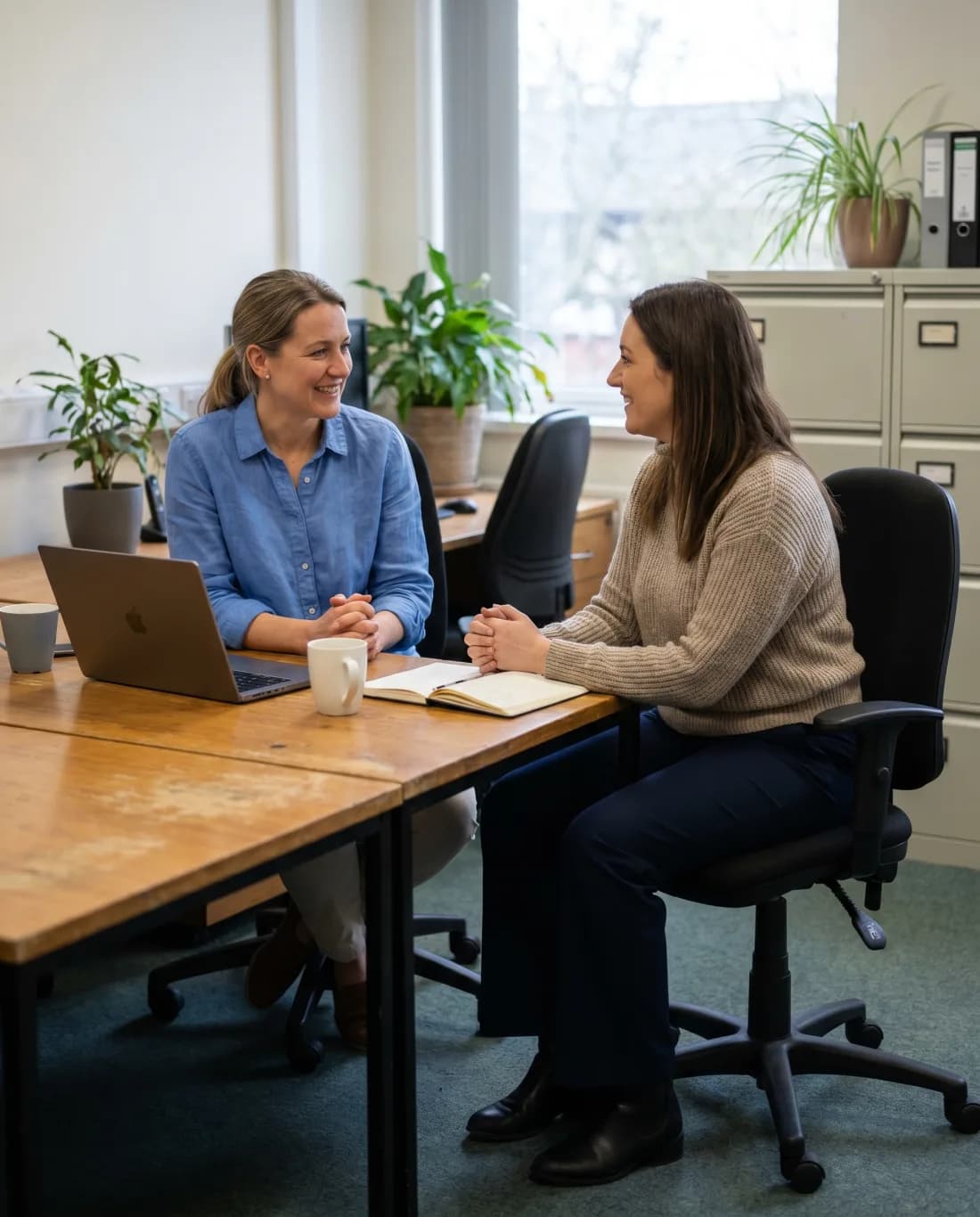 A wellness facilitator and an HR manager in a calm conversation in a bright office lounge. Illustrative.